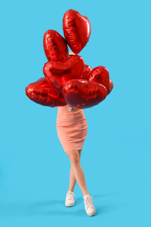 Beautiful young woman with heart-shaped balloons on blue background. Valentine's Day celebrationの写真素材