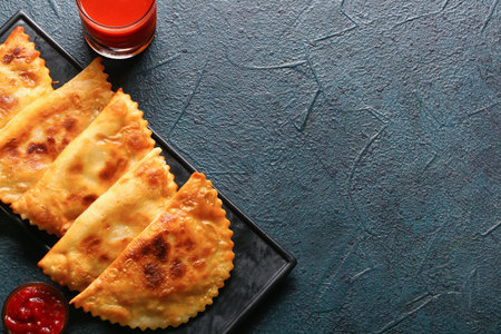 Board with tasty chebureks and tomato juice on grunge background