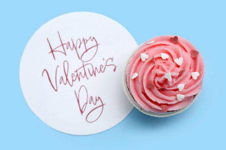 Tasty cupcake and card with text HAPPY VALENTINE'S DAY on blue backgroundの写真素材