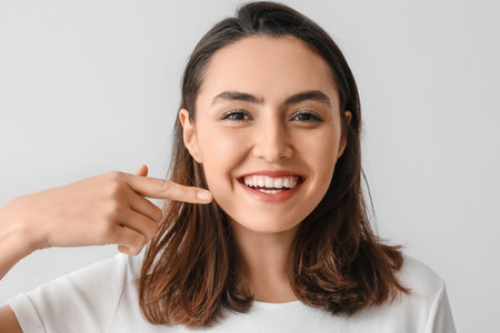 Young woman pointing at her teeth on gray background, closeup