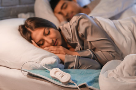 Young couple sleeping on electric heating pad in bedroom at nightの写真素材