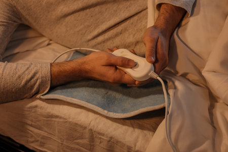 Young man turning on electric heating pad in bedroom at night, closeupの写真素材
