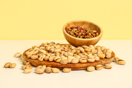 Board and bowl with tasty pistachio nuts on yellow backgroundの写真素材