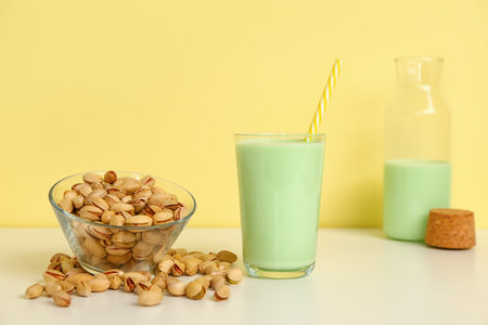 Glass of pistachio milk and bowl with nuts on yellow backgroundの写真素材