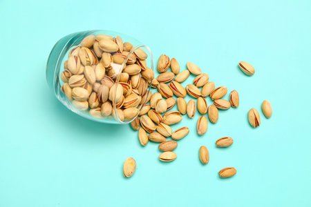 Overturned glass with tasty pistachio nuts on blue backgroundの写真素材