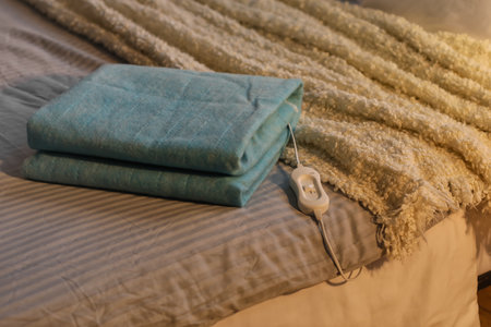 Folded electric heating pad with controller on bed in dark room, closeupの写真素材