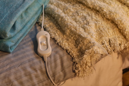 Folded electric heating pad with controller on bed in dark room, closeup
