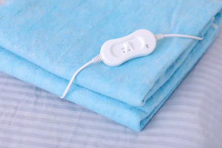 Folded electric heating pad with controller on bed in room, closeupの写真素材