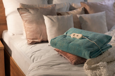 Bed with pillows and folded electric heating pad in the bedroom at nightの写真素材