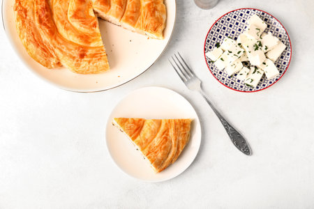 Plates with delicious cheese pie and ingredients on white table