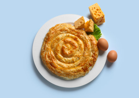 Plate with delicious cheese pie and ingredients on blue backgroundの写真素材