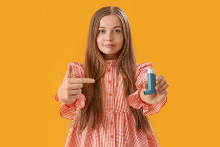 Young woman with inhaler on yellow background