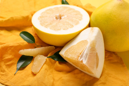 Kitchen towel with pomelo fruit and slices on light yellow background, closeup