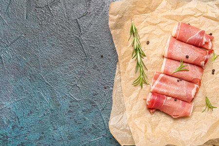Baking paper with slices of tasty ham and rosemary on dark color backgroundの写真素材