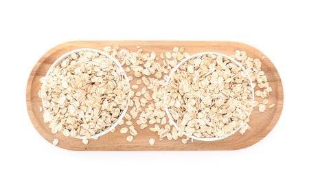 Wooden board with bowls of raw oatmeal on white background