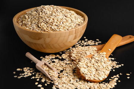 Bowl and spoons of raw oatmeal on dark background, closeup
