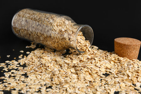 Overturned bottle of raw oatmeal on dark background, closeupの写真素材