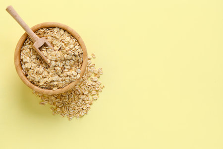 Wooden bowl of raw oatmeal on yellow backgroundの写真素材