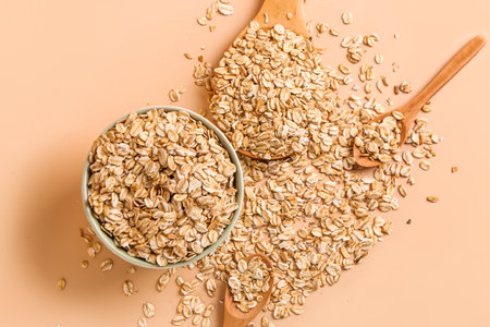 Bowl and spoons of raw oatmeal on color background, closeup