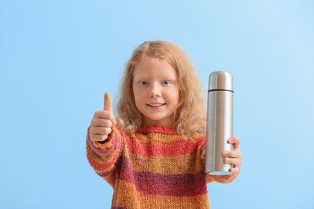 Little redhead girl with bottle showing thumb-up on blue backgroundの写真素材