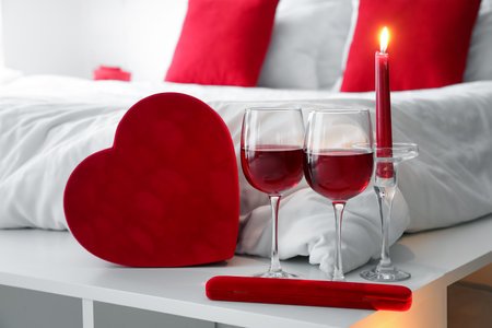 Glasses of wine, burning candle and gifts for Valentine's Day on shelf in bedroomの写真素材