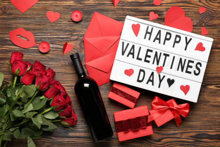 Board with text HAPPY VALENTINE'S DAY, bottle of wine, envelopes, gifts and roses on wooden backgroundの写真素材