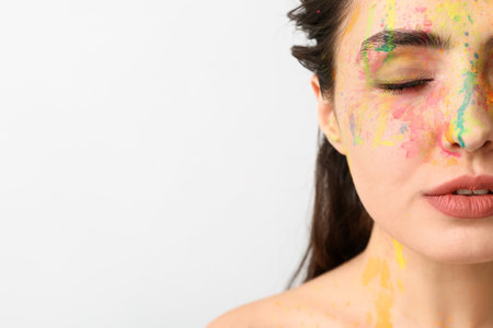 Beautiful young woman with paint on her face against light backgroundの写真素材