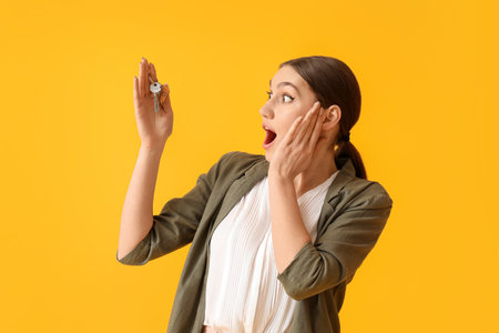 Surprised young woman with key from house on color backgroundの写真素材