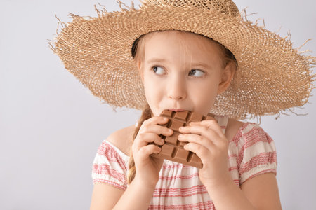 Cute little girl eating chocolate on light background, closeupの写真素材