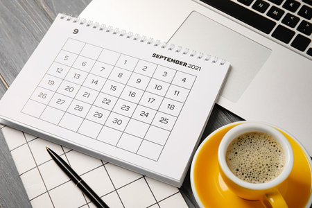 Flip paper calendar with laptop, cup of coffee and stationery on tableの写真素材