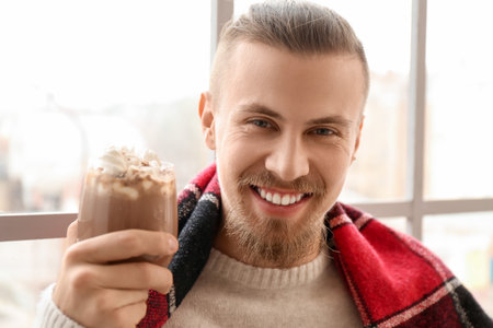 Handsome man with cup of hot cocoa near window at homeの写真素材