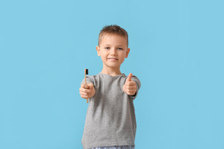 Little boy with toothbrush showing thumb-up on color backgroundの写真素材