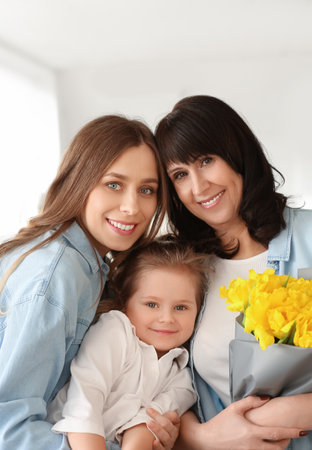 Young woman, her little daughter and mother with bouquet of flowers at home