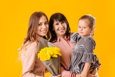 Young woman, her little daughter and mother with bouquet of flowers on color backgroundの写真素材