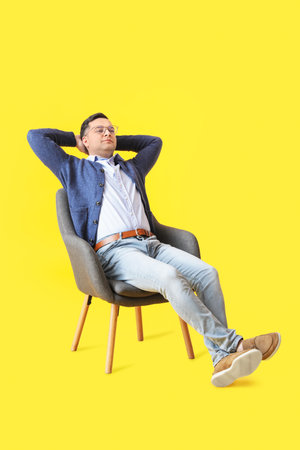 Young man sitting in armchair on color backgroundの写真素材