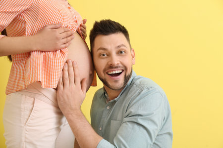 Beautiful pregnant couple on color backgroundの写真素材