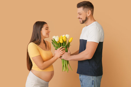 Beautiful pregnant couple with bouquet of flowers on color backgroundの写真素材