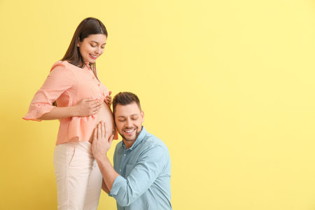 Beautiful pregnant couple on color backgroundの写真素材