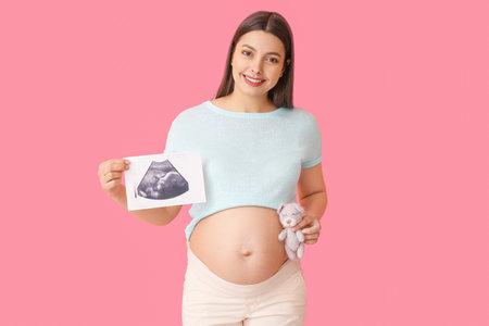 Young pregnant woman with sonogram image and toy on color backgroundの写真素材