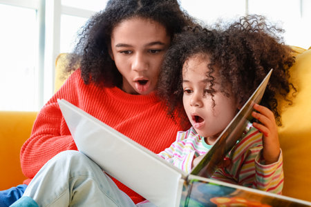 Cute African-American sisters reading book at homeの写真素材