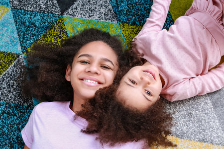 Cute African-American sisters lying on carpet, top viewの写真素材
