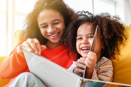 Cute African-American sisters reading book at homeの写真素材