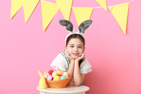 Cute little girl with bunny ears and Easter eggs on color background