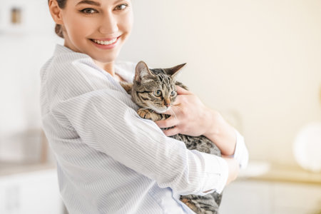 Beautiful young woman with cute cat in the kitchenの写真素材
