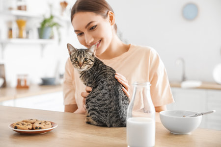 Beautiful young woman with cute cat in the kitchenの写真素材