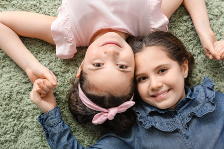 Portrait of cute twin girls lying on carpet, top viewの写真素材