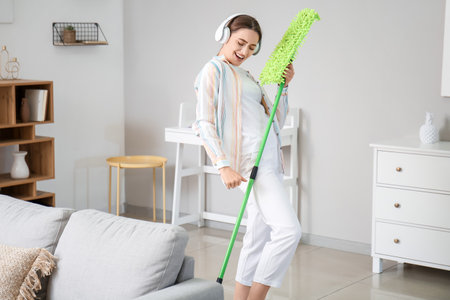 Young woman listening to music while mopping floor in room