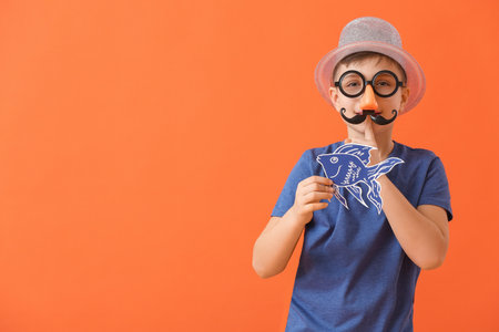 Little boy with paper fish showing silence gesture on color background. April Fools Day celebrationの写真素材