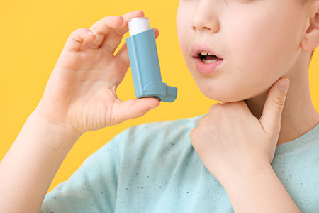 Little boy with inhaler having asthma attack on color background, closeup