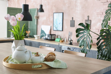 Tray with tasty muffins, teapot and vase on table in kitchenの写真素材